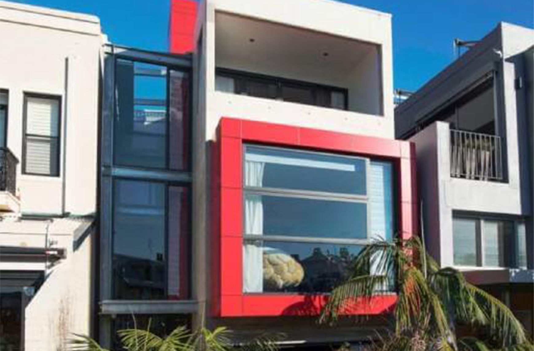 Modern multi-storey townhouse with a red-framed window and glass facade