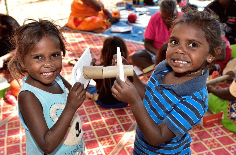 Two young children smiling and holding a craft made from cardboard tubes at an outdoor learning session