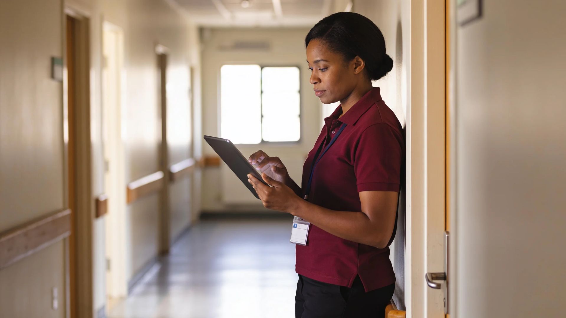 Staff member in a polo shirt with a lanyard badge using a tablet in a corridor