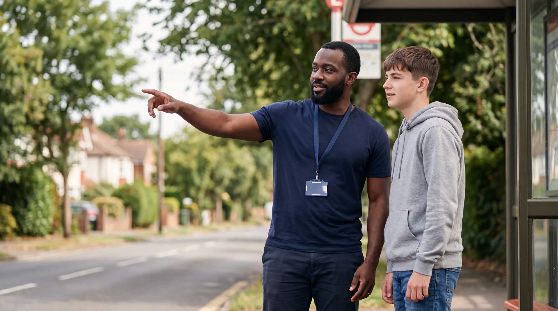 Staff member pointing down the street beside a teenager at a bus stop