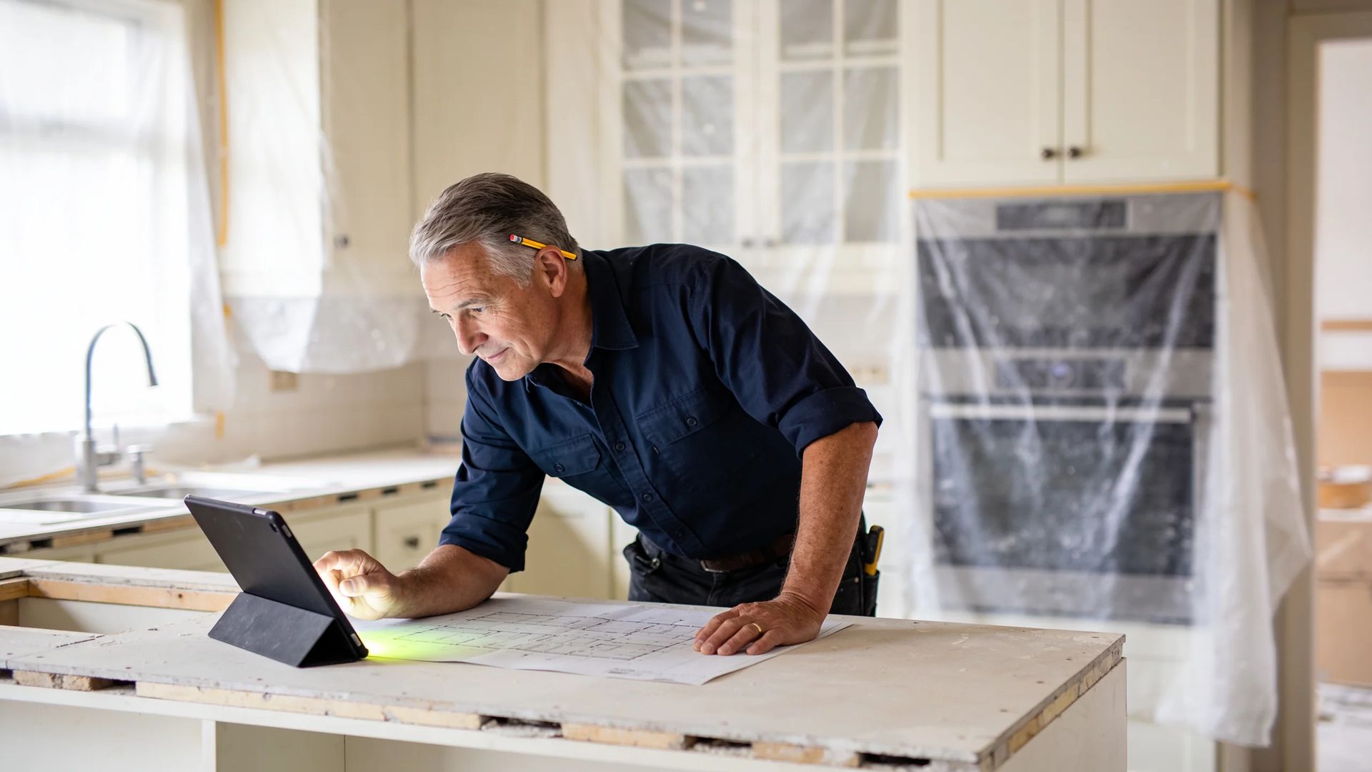 Worker looking at a tablet and plans on a kitchen counter during a renovation