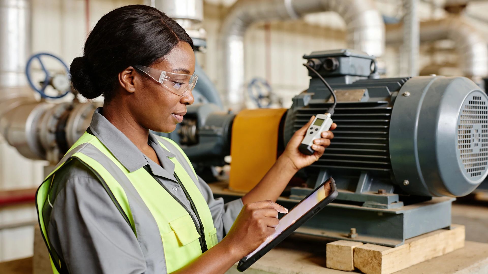 Technician holding a handheld meter and a tablet beside a motor