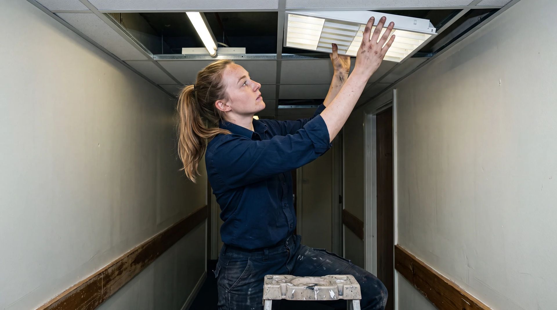 Technician on a stepladder fitting a light diffuser into a ceiling grid