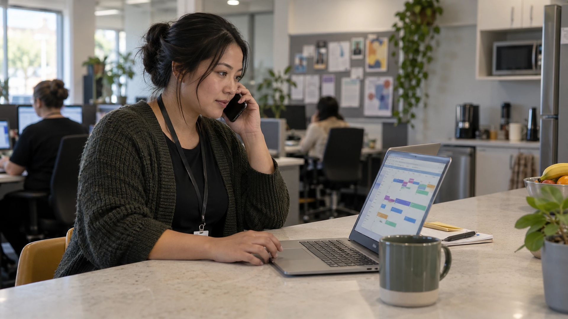 Office worker on a mobile phone call using a laptop at an office bench