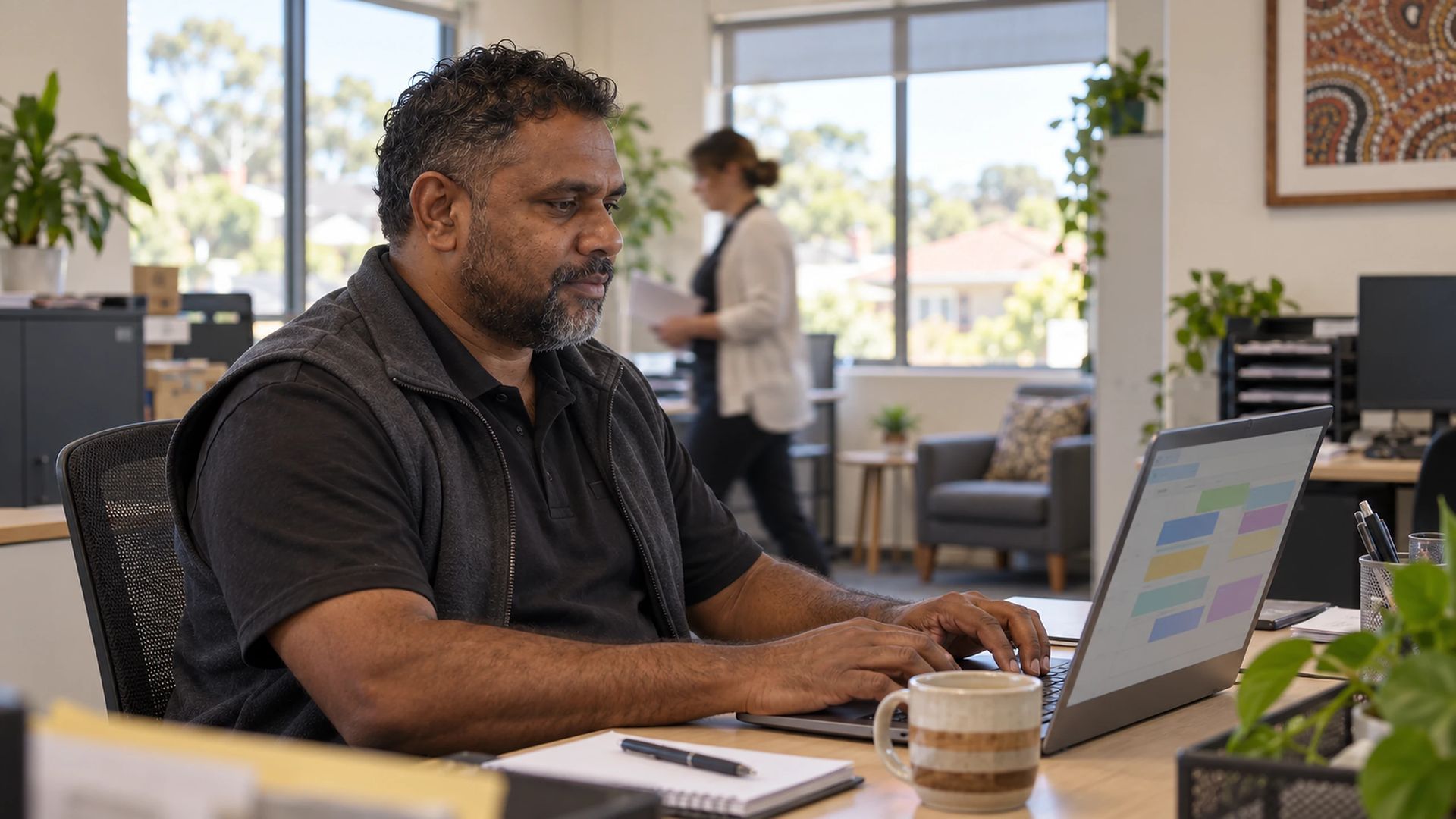 Office worker using a laptop, a colleague passing behind