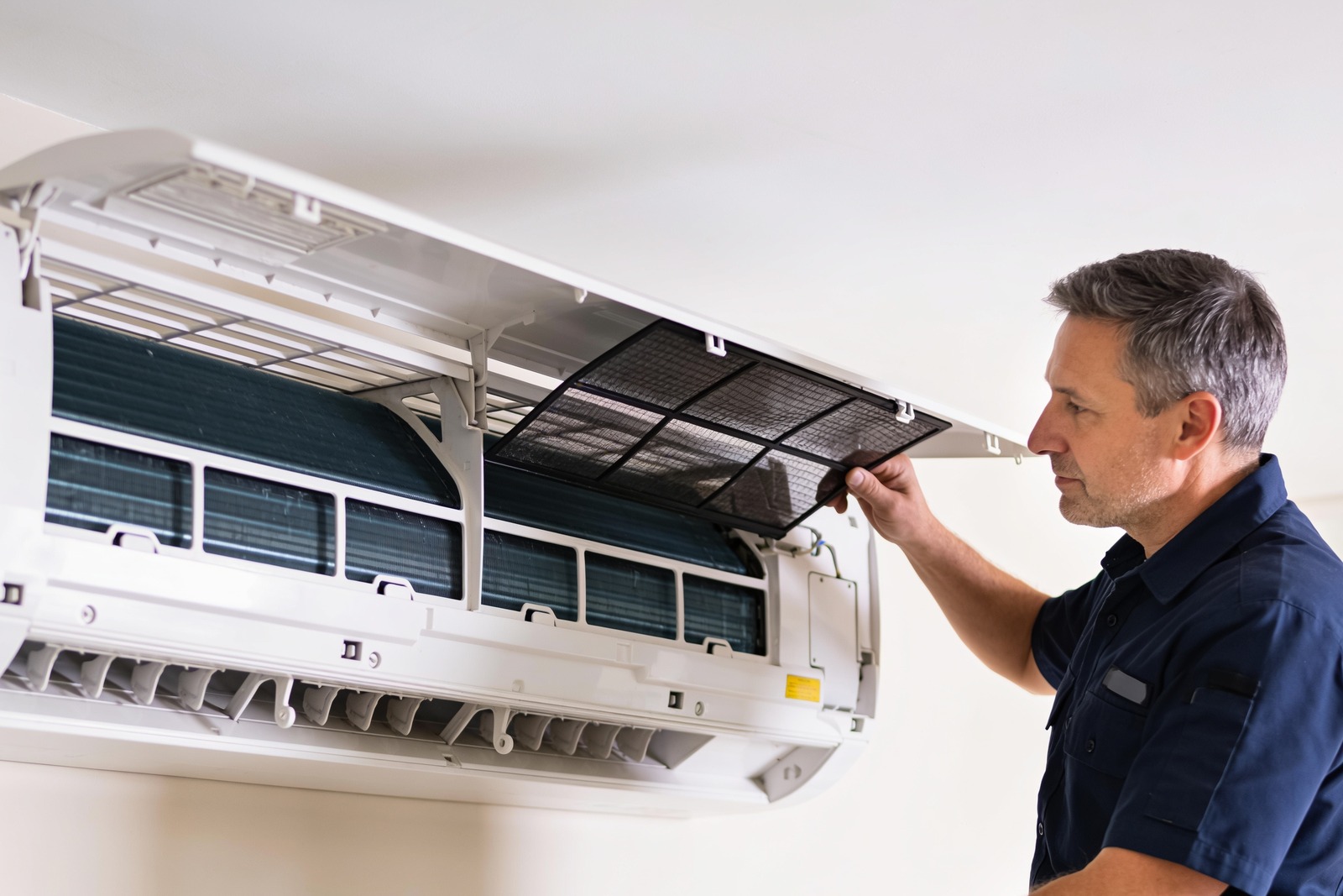 HVAC technician lifting the filter on a wall-mounted unit